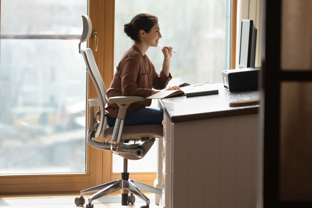 Mulher de cabelo preso sentada em cadeira ergonômica e de frente para monitor de computador