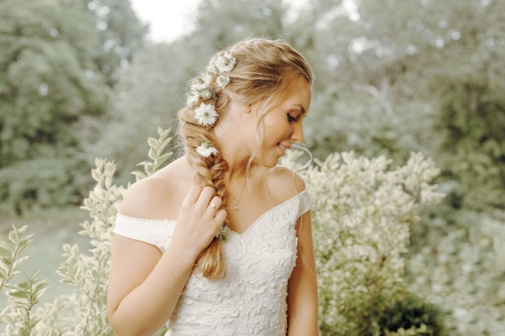 Mulher com cabelo loiro preso em tranças com flores, usando vestido de noiva em jardim